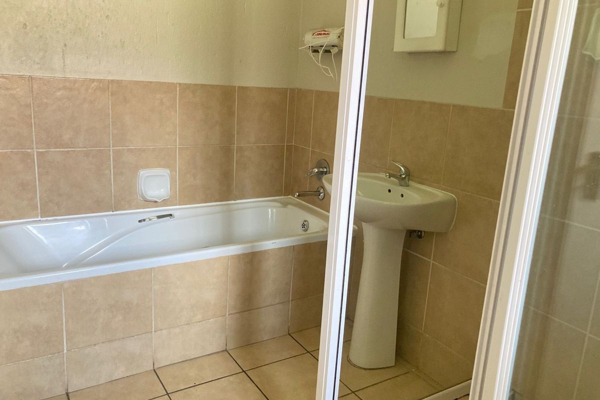 A functional bathroom featuring a built-in bathtub, pedestal basin, and tiled walls and flooring.