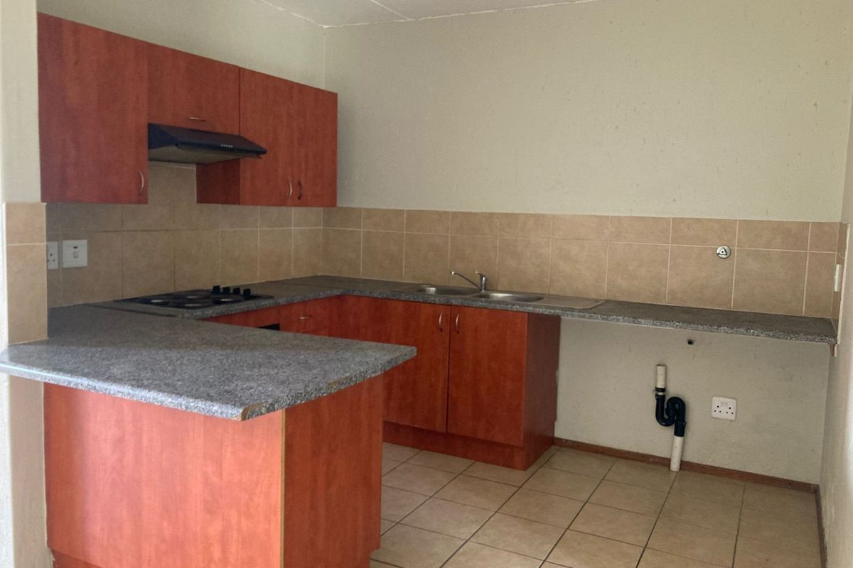 A functional kitchen featuring wood-look cabinetry, granite-style countertops, a built-in hob, extractor fan, and tiled splashbacks with space for under-counter appliances.