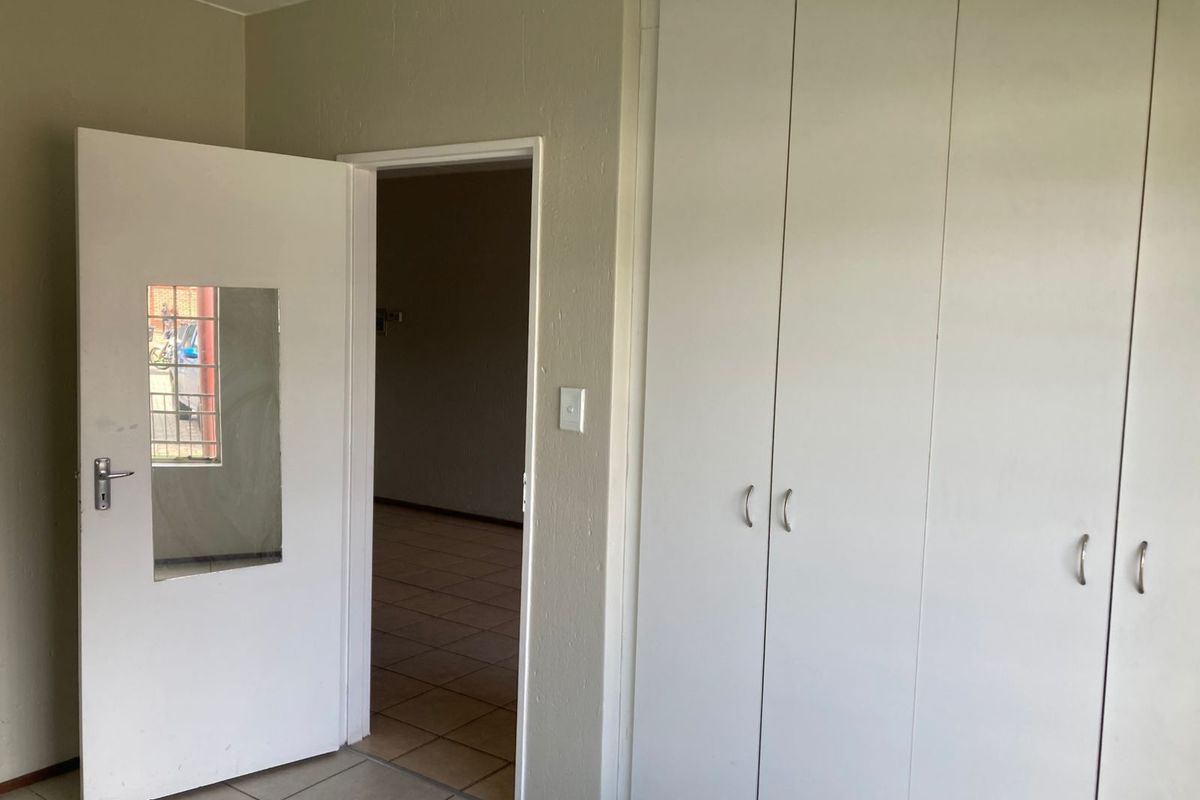 A bedroom interior featuring built-in white cabinetry and tiled flooring, with a doorway leading to an adjacent living area.