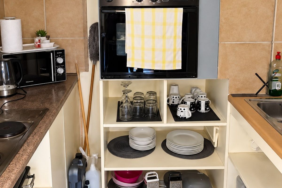 Compact kitchen featuring a built-in Miele oven, ceramic hob, tiled backsplash, and open shelving storage with neutral floor tiling.
