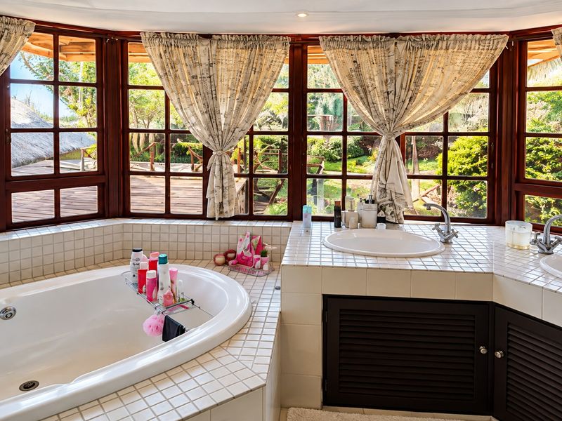 A bright bathroom featuring a built-in bathtub, dual vanity with tiled countertop, and large timber-framed windows overlooking a garden.