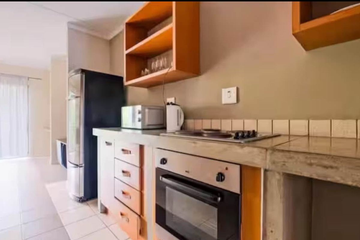 A functional kitchen featuring concrete countertops, built-in oven, electric hob, and wooden cabinetry with open shelving.