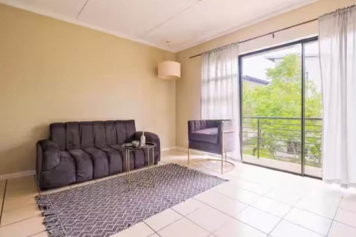 A bright living room featuring tiled flooring and a large sliding glass door that provides direct access to an outdoor balcony.