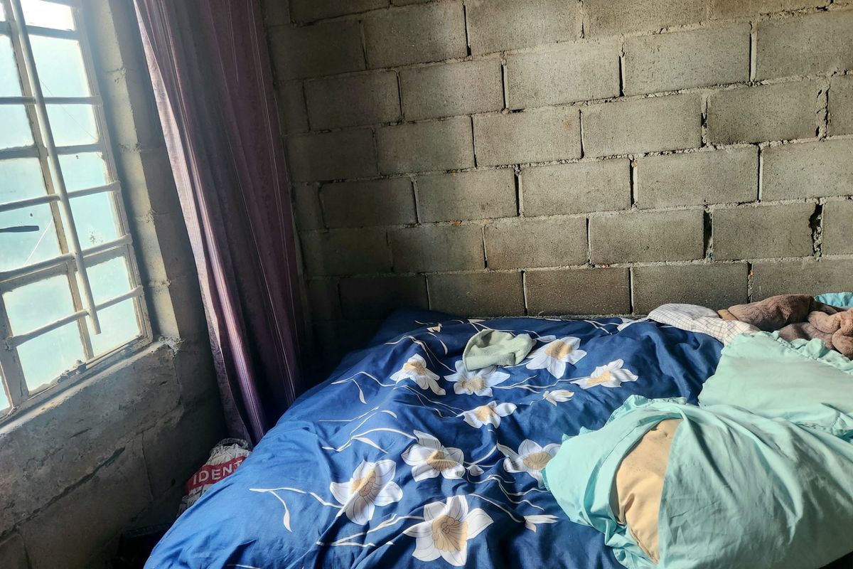 A bedroom featuring exposed concrete block walls and a metal-framed window, currently requiring interior finishing and renovation.