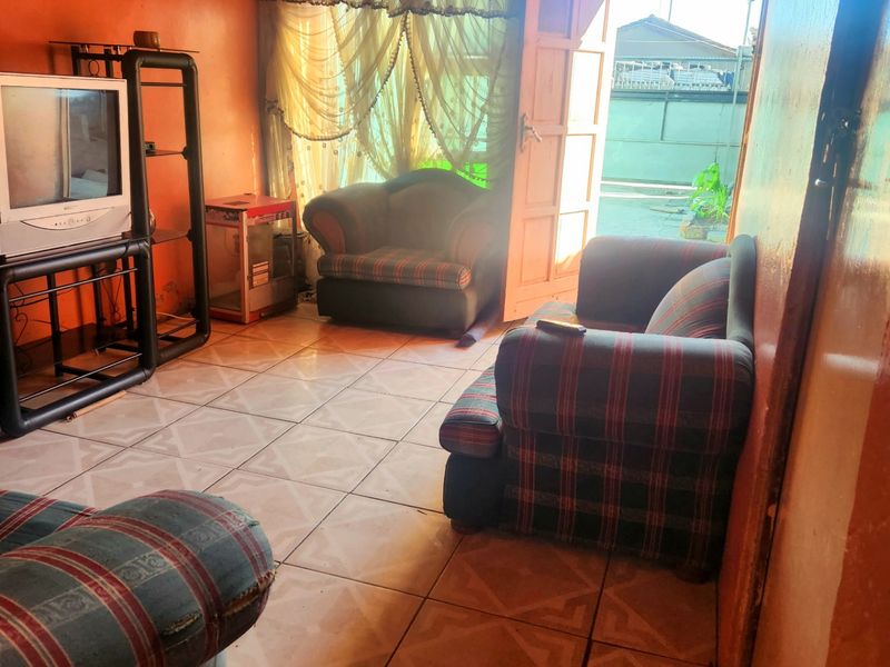 A living room area featuring tiled flooring and direct access to the exterior, requiring cosmetic updates to the walls and ceiling.
