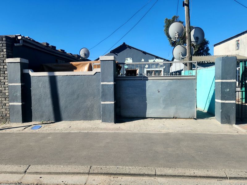 Front view of the property featuring a grey boundary wall, sliding gate, and visible satellite dishes mounted on a utility pole.