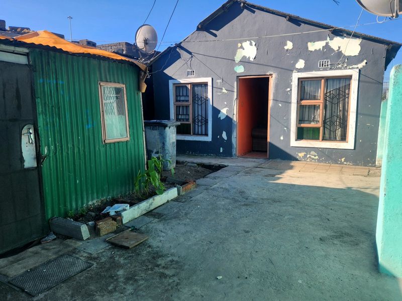 Rear exterior view of a house featuring a corrugated metal outbuilding, concrete yard, and visible wear to the main building's exterior paintwork.