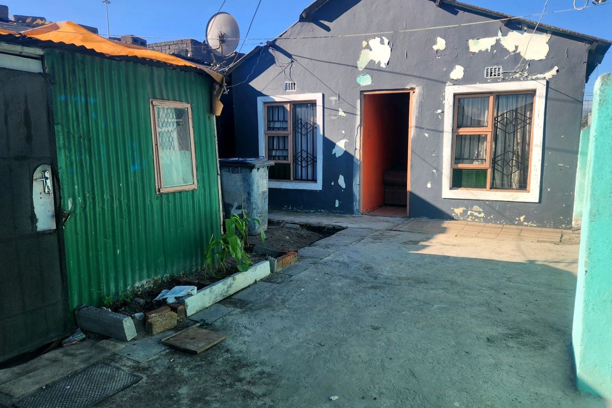 Rear exterior view of a house featuring a corrugated metal outbuilding, concrete yard, and visible wear to the main building's exterior paintwork.