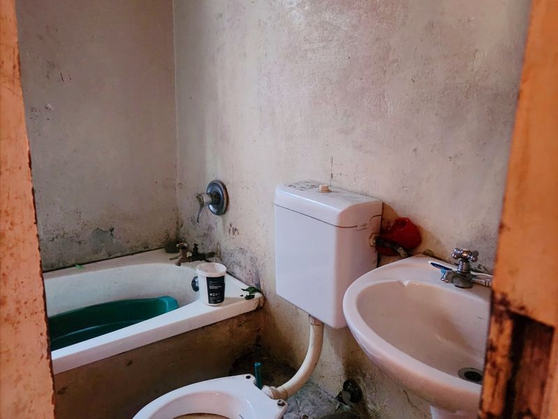A small, dated bathroom featuring a bathtub, pedestal basin, and toilet, requiring significant renovation and cosmetic updates to improve its condition.