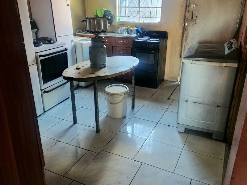 A functional kitchen space featuring tiled flooring, built-in cabinetry, and a window with security bars, requiring cosmetic updates to improve its overall condition.