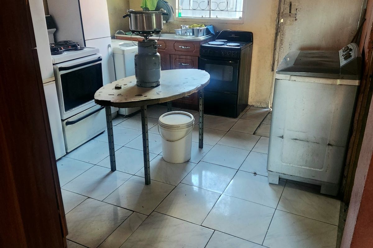 A functional kitchen space featuring tiled flooring, built-in cabinetry, and a window with security bars, requiring cosmetic updates to improve its overall condition.