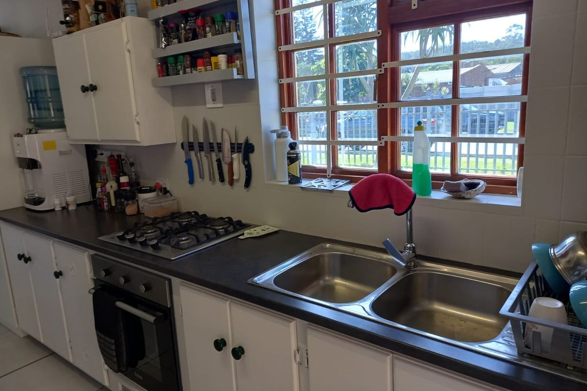 A functional kitchen featuring white cabinetry, a gas hob, built-in oven, and a double bowl stainless steel sink with a window view.