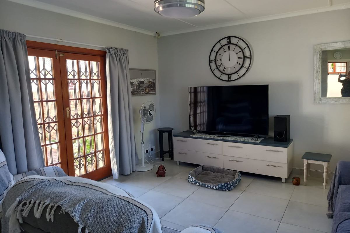 A living room featuring tiled flooring and wooden framed glass double doors with security gates, providing access to the exterior.