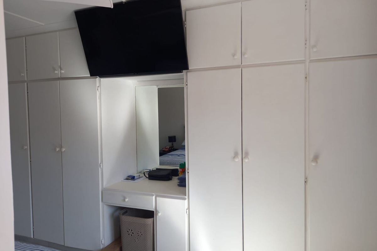 Bedroom featuring extensive white built-in cupboards with integrated vanity desk and mirror, providing ample storage space.