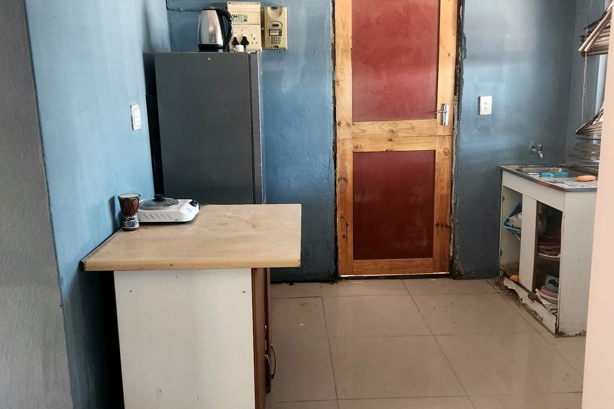 A basic kitchen area featuring tiled flooring, a sink unit, and a timber door, requiring cosmetic updates and maintenance to improve functionality and aesthetic appeal.