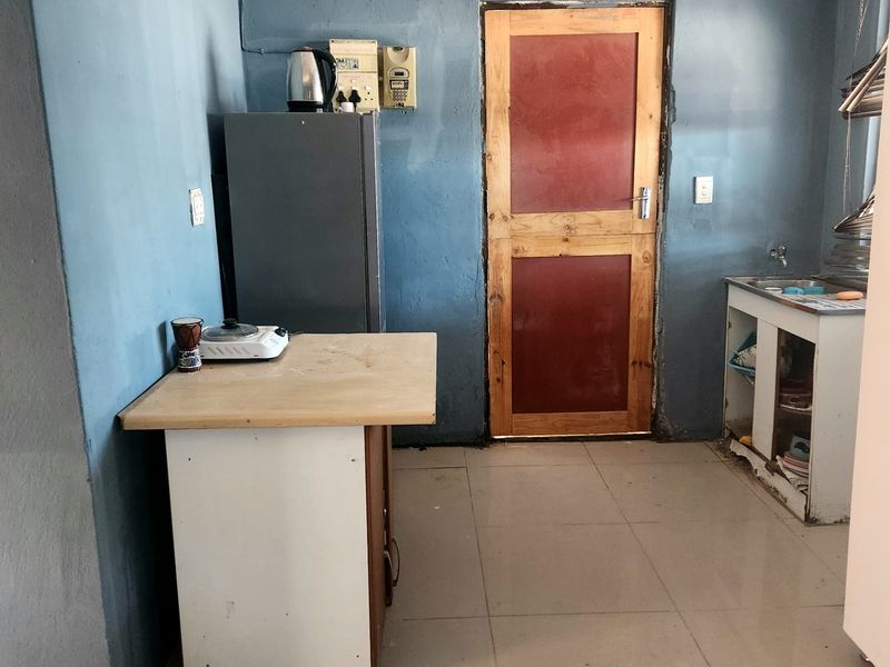 A basic kitchen area featuring tiled flooring, a sink unit, and a timber door, requiring cosmetic updates and maintenance to improve functionality and aesthetic appeal.