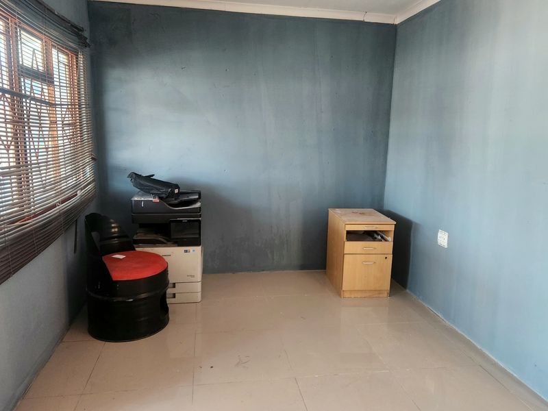 A small, sparsely furnished office space featuring tiled flooring and blue painted walls, suitable for a home workspace or study.