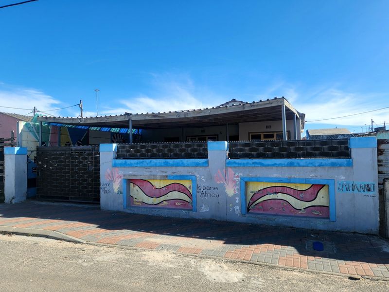 Front view of a residential property featuring a painted boundary wall, metal gate, and a covered patio area.