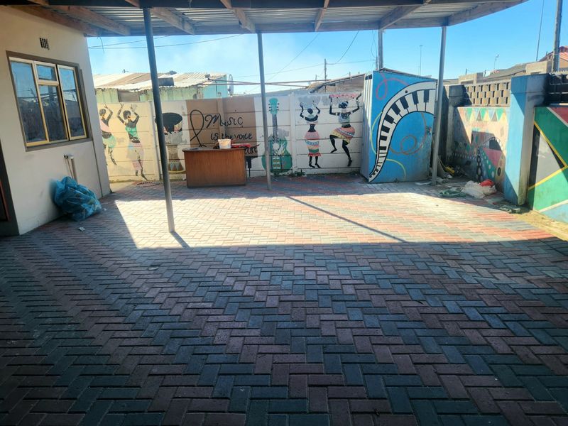 A paved, covered outdoor patio area featuring a boundary wall with decorative murals, providing a functional space for outdoor activities.