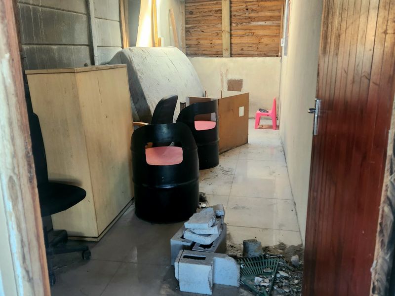 An unfinished utility space featuring tiled flooring, exposed timber roof structure, and concrete block walls, currently used for storage.