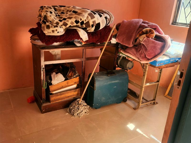 A small bedroom space featuring tiled flooring and a window with security bars, currently used for storage.