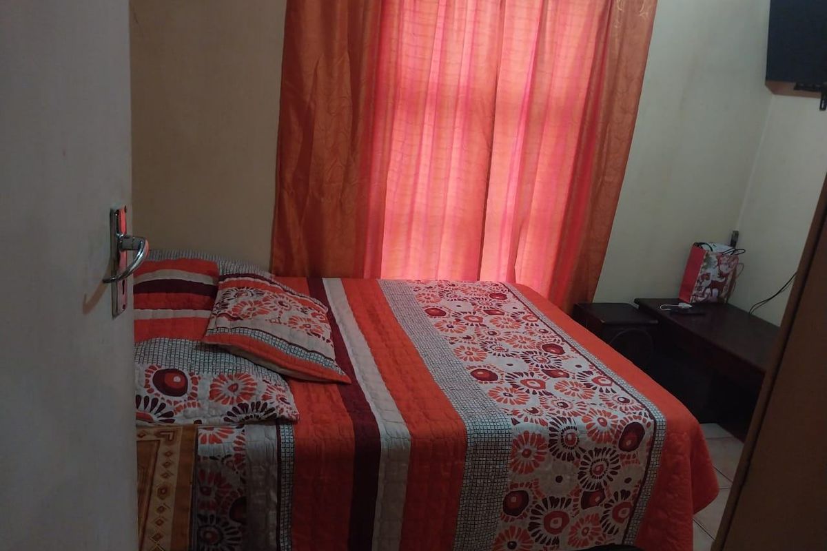 A standard bedroom featuring tiled flooring and a window with curtains, providing a functional sleeping space.