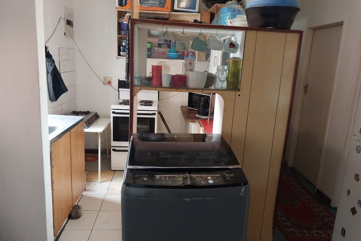 A functional kitchen area featuring tiled flooring, built-in cabinetry, and a freestanding stove, currently showing signs of age and wear.