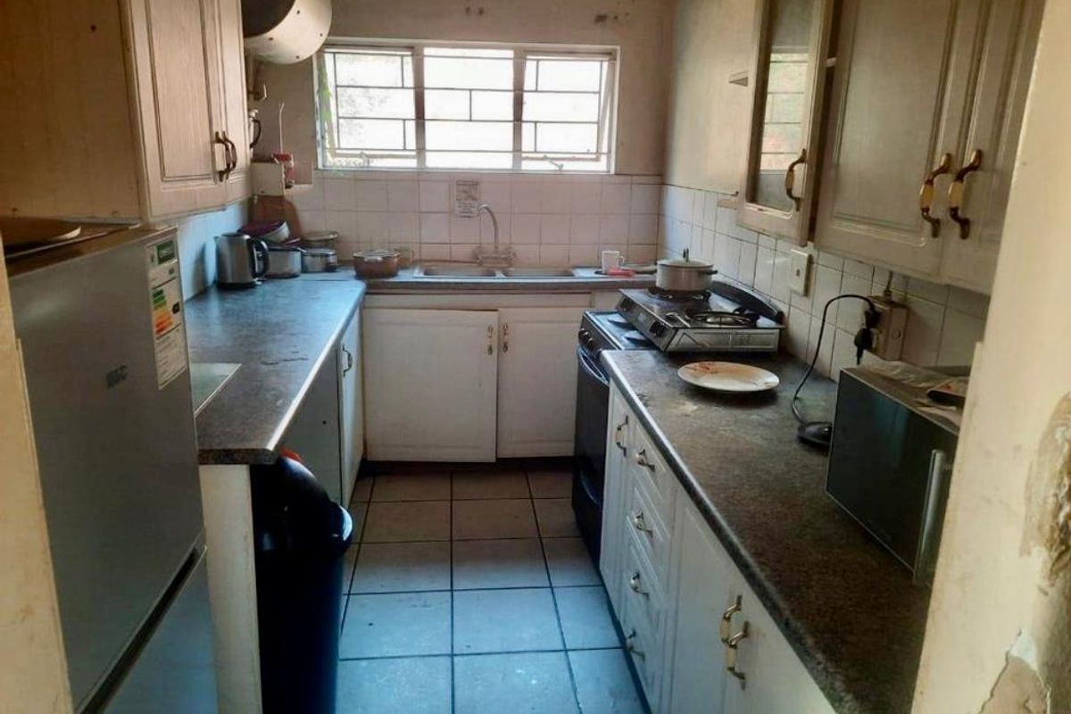 A compact, dated kitchen featuring laminate countertops, tiled backsplash, and built-in cabinetry, requiring cosmetic updates to modernize the space.