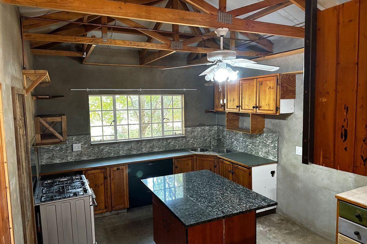 Rustic kitchen featuring exposed timber roof trusses, a central island with granite countertop, gas stove, and timber cabinetry with a tiled backsplash.