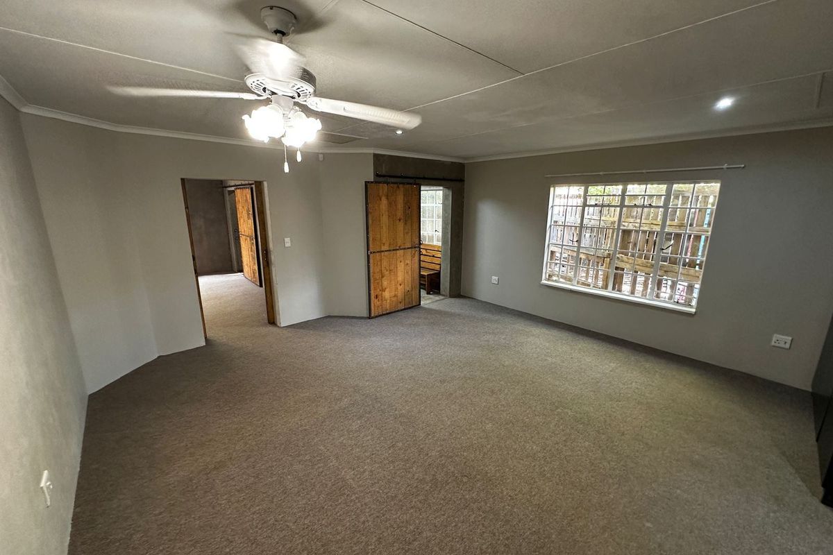 Spacious living area featuring neutral walls, carpet flooring, a ceiling fan, and rustic sliding barn doors leading to adjacent rooms.