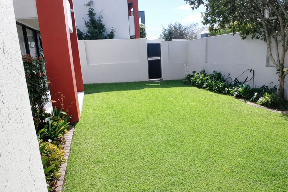 A well-maintained private rear garden featuring a manicured lawn, perimeter boundary walls, and established garden beds.