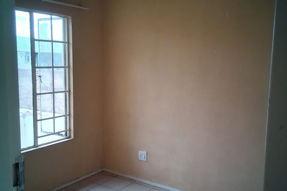 A compact, empty bedroom featuring tiled flooring, a window with security bars, and neutral wall paint, offering a blank canvas for potential updates.