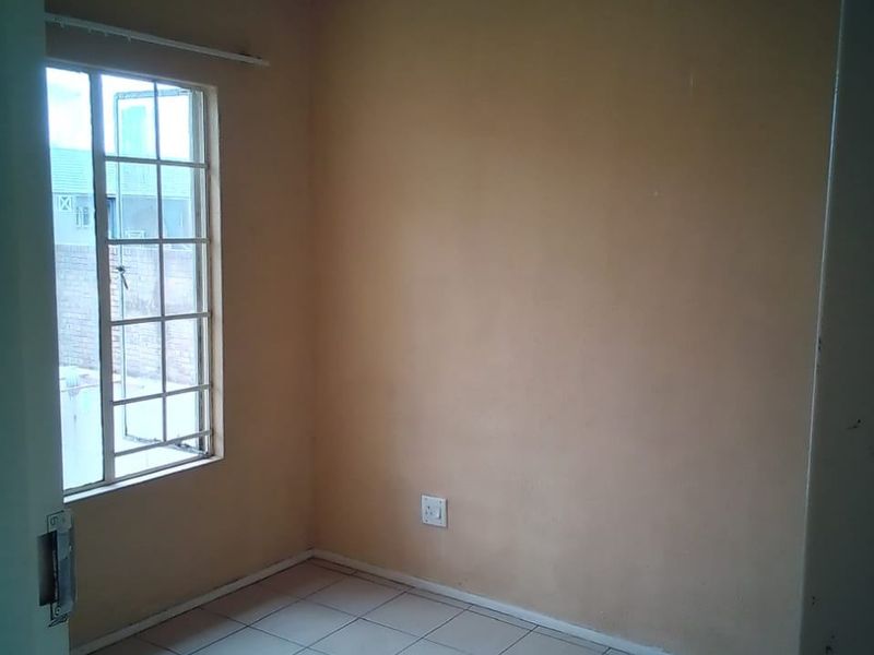 A compact, empty bedroom featuring tiled flooring, a window with security bars, and neutral wall paint, offering a blank canvas for potential updates.
