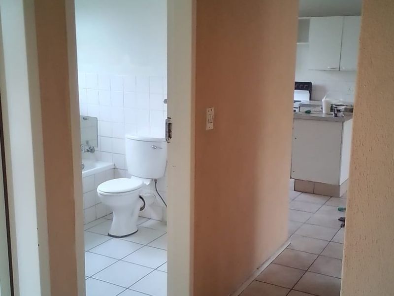 A view from the hallway looking into a bathroom with tiled flooring and a kitchen area featuring white cabinetry and countertops.