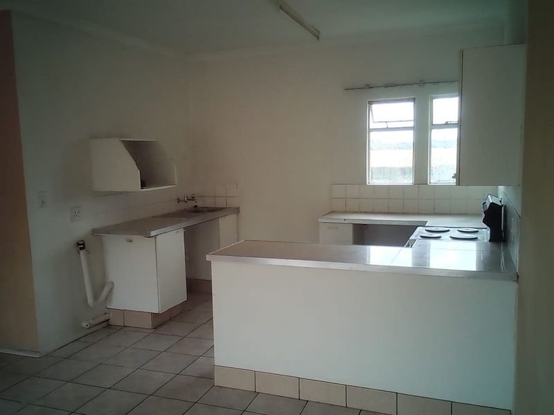 An empty, dated kitchen featuring built-in cabinetry, laminate countertops, a stainless steel sink, and an electric hob, ready for renovation.