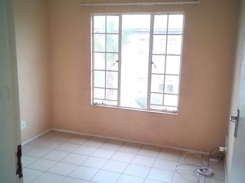 An empty bedroom featuring tiled flooring, a grid-pattern window with a curtain rod, and neutral wall paint.