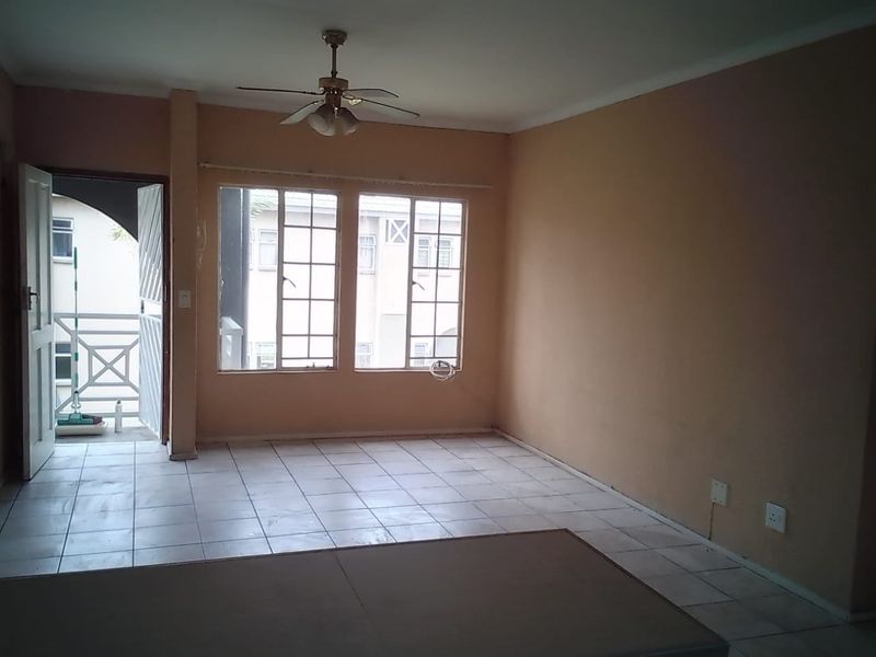 An empty living room featuring tiled flooring, a ceiling fan, and direct access to an outdoor balcony area.