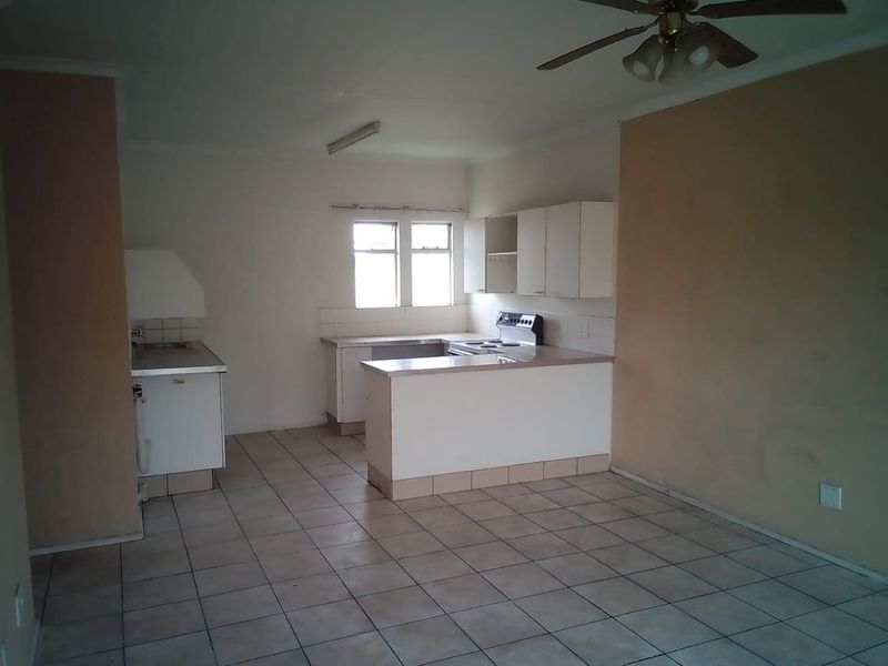 An open-plan kitchen and living area featuring tiled flooring, built-in cabinetry, and an electric stove, offering a blank canvas for renovation.