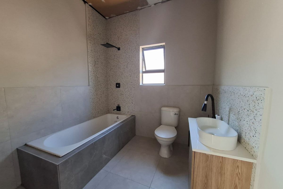 A modern bathroom featuring a built-in bathtub, terrazzo-style tiling, and a vanity unit, currently awaiting final ceiling completion.