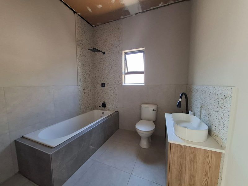 A modern bathroom featuring a built-in bathtub, terrazzo-style tiling, and a vanity unit, currently awaiting final ceiling completion.