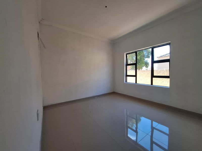 An empty bedroom featuring tiled flooring, white walls, and an aluminium window frame, providing a blank canvas for personalization.