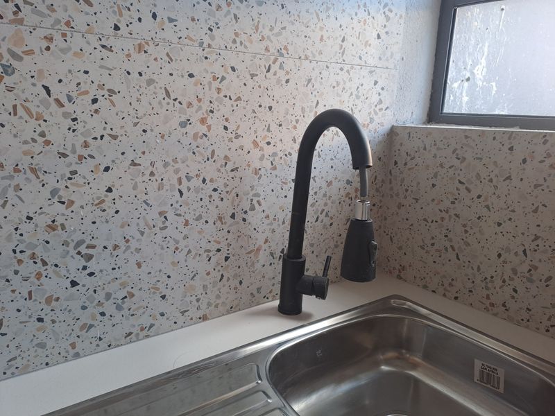 Close-up of a kitchen sink area featuring a modern matte black pull-down faucet and a decorative terrazzo-style tiled backsplash.