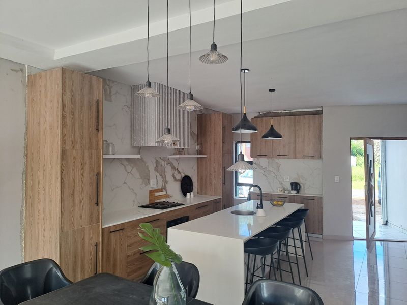 Modern kitchen featuring wood-grain cabinetry, stone countertops, a central island with sink, and marble-look splashback, complemented by stylish pendant lighting.