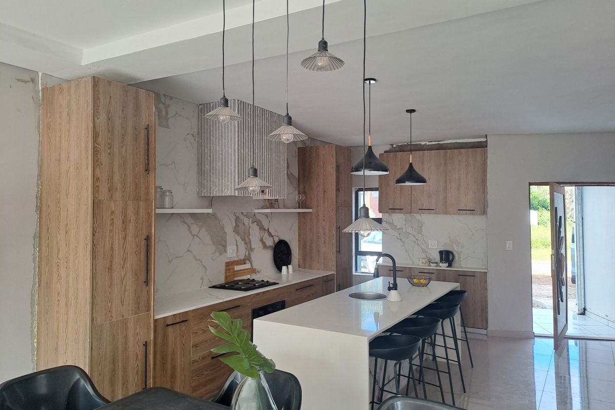 Modern kitchen featuring wood-grain cabinetry, stone countertops, a central island with sink, and marble-look splashback, complemented by stylish pendant lighting.