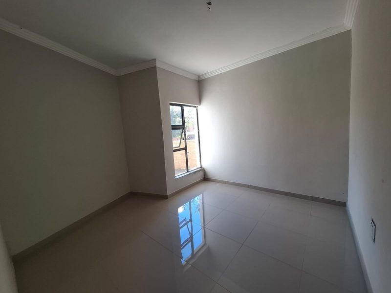A bright, empty bedroom featuring neutral walls, polished tiled flooring, and a modern aluminium window frame.