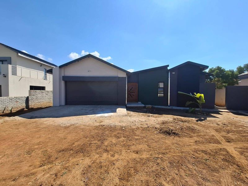 Modern single-story residential facade featuring a double garage, dark exterior cladding, and a timber entrance door, set on an unlandscaped plot.