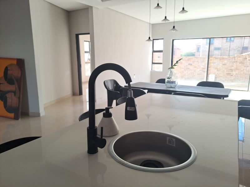 Modern open-plan living area featuring a kitchen island with a sleek sink, pendant lighting, and large sliding doors leading to the rear exterior.