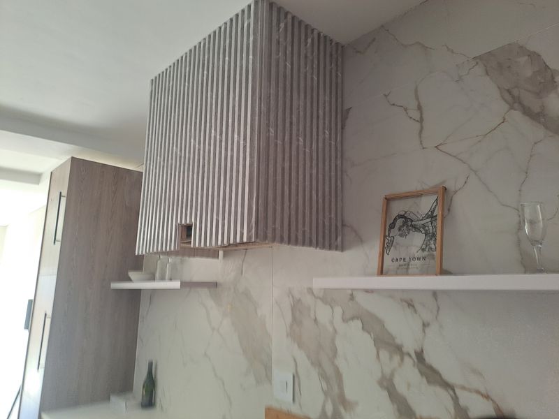 Modern kitchen featuring a textured extractor fan housing, marble-look wall tiling, and sleek built-in cabinetry with floating shelving.