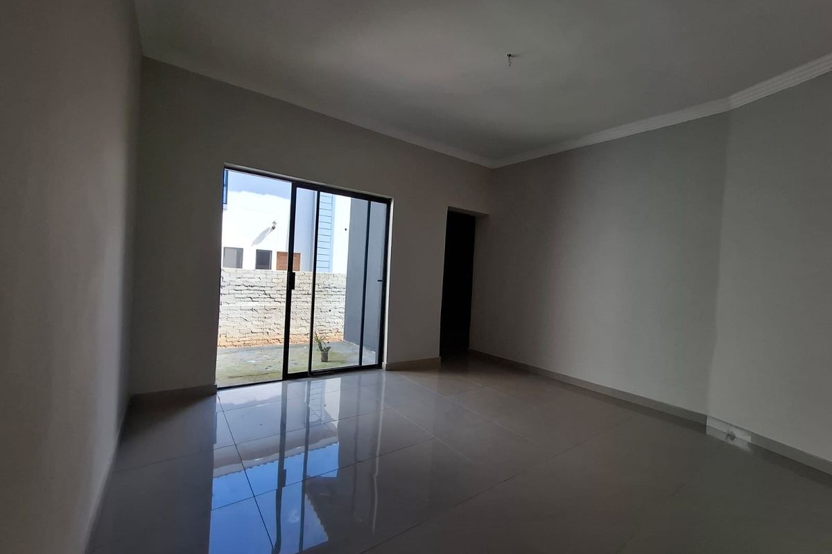 A bright, empty living room featuring neutral tiled flooring and a large sliding glass door providing access to the rear exterior area.