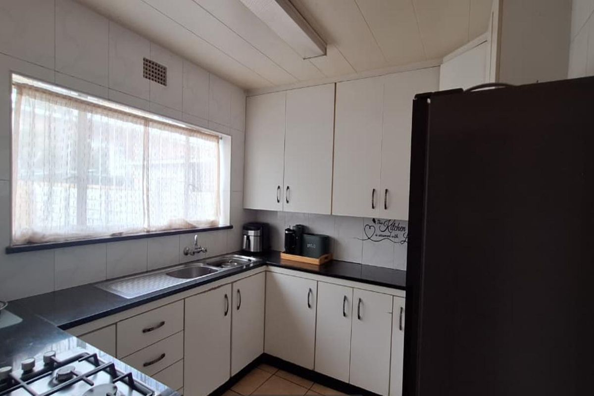 A functional kitchen featuring white cabinetry, dark countertops, a stainless steel sink, and a built-in gas hob, offering a practical layout for daily use.